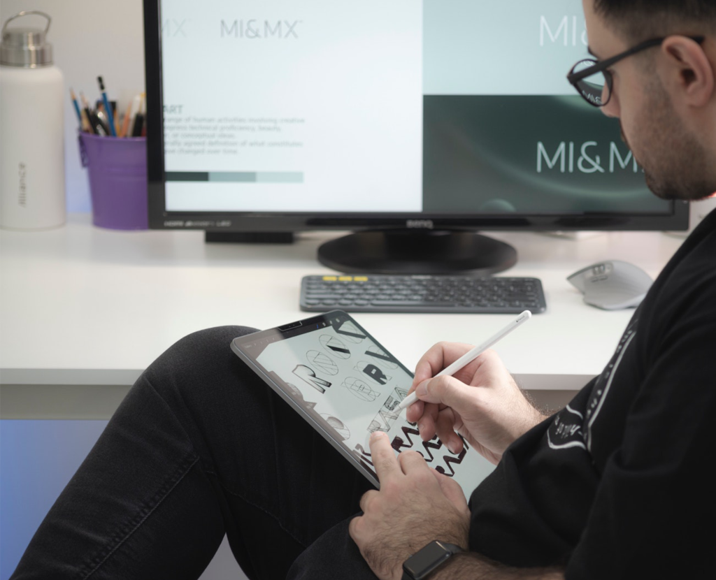 Logo Designer sketching concepts for a modern brand identity with a mac and iPad Pro in his workspace.